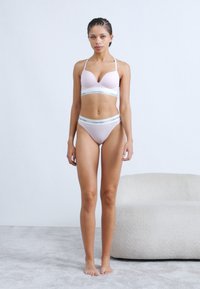 Ροζ ανοιχτό ροζ σουτιέν με λεπτές τιράντες και καλουπωμένα cups, σετ με αντίστοιχα εσώρουχα ψηλόμεσα με λευκή ζώνη μέσης με το λογότυπο Calvin Klein.