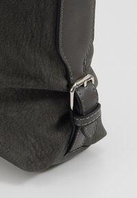Angolo di una borsa in finta pelle grigia, con una superficie texture, fibbia in metallo argentato e cuciture a contrasto sulla tracolla.