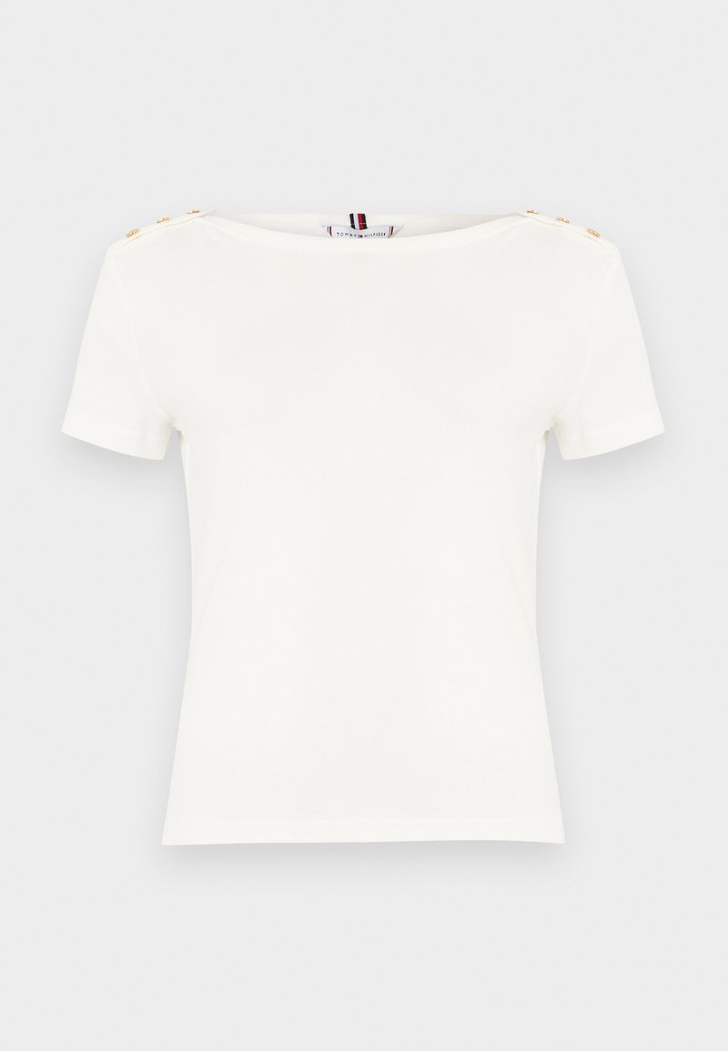 Άσπρο γυναικείο τοπ με κοντά μανίκια, λαιμόκοψη τύπου βάρκα και χρυσά κουμπιά στους δύο ώμους, σε απλό ανοιχτό φόντο.