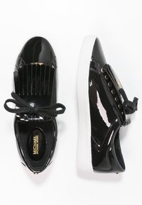 Schwarze Lackledersneakers mit weißen Sohlen, schwarzen Schnürsenkeln, Fransen-Detail an der Vorderseite und goldenem Michael Kors-Logo im Inneren.