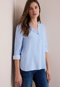 Ljusblå skjortblus med V-ringning, uppvikta ärmar och vertikala ränder. Mjuk tyg med en avslappnad passform. Stylad med blå jeans.