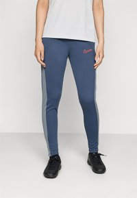Mørkeblå leggins med grå sidestykker, med en rød Nike-logo. Laget av elastisk stoff, med en tettsittende design og elastisk midjebånd.