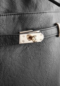 Zwarte leren handtas met een getextureerd oppervlak, voorzien van een glanzende gouden metalen sluiting en een zwarte riem met zichtbare stiksels.