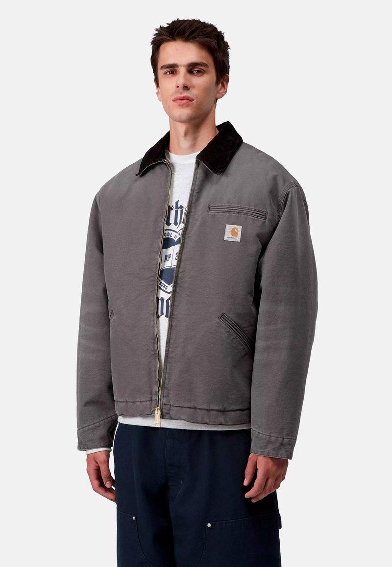 Gray cotton jacket with a black corduroy collar, front zipper, chest pocket, and side pockets. Worn over a gray graphic t-shirt.