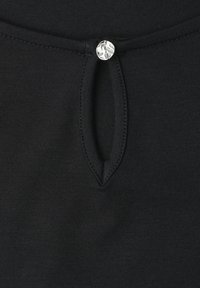 Tissu noir avec un petit décolleté œillet fermé par un seul bouton argenté brillant.
