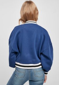 Blue cropped sweatshirt with a relaxed fit, featuring white and black striped trim on the collar and hem. Soft texture, minimal detailing.