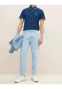 Laivaston sininen poolopaita valkoisilla reunuksilla, vaaleansiniset farkut, ja vaaleansinistä farkkutakkia pitelevä. Valkoiset tennarit täydentävät rentoa asua.