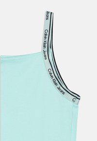 Világoskék ujjatlan póló fekete-fehér logós pánttal, amelyen a "Calvin Klein Jeans" felirat szerepel. Simak felület és testhez álló fazon.