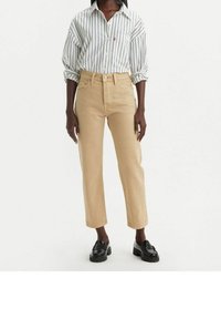 Jeans de pierna recta beige con cintura alta, hechos de denim resistente. Combinados con una camisa de manga larga a rayas blancas. Mocasines negros en los pies.