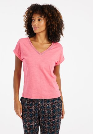 Roze V-hals t-shirt met opgerolde korte mouwen, gemaakt van lichtgewicht stof. Losvallende broek in donkere kleuren met bloemige patronen.