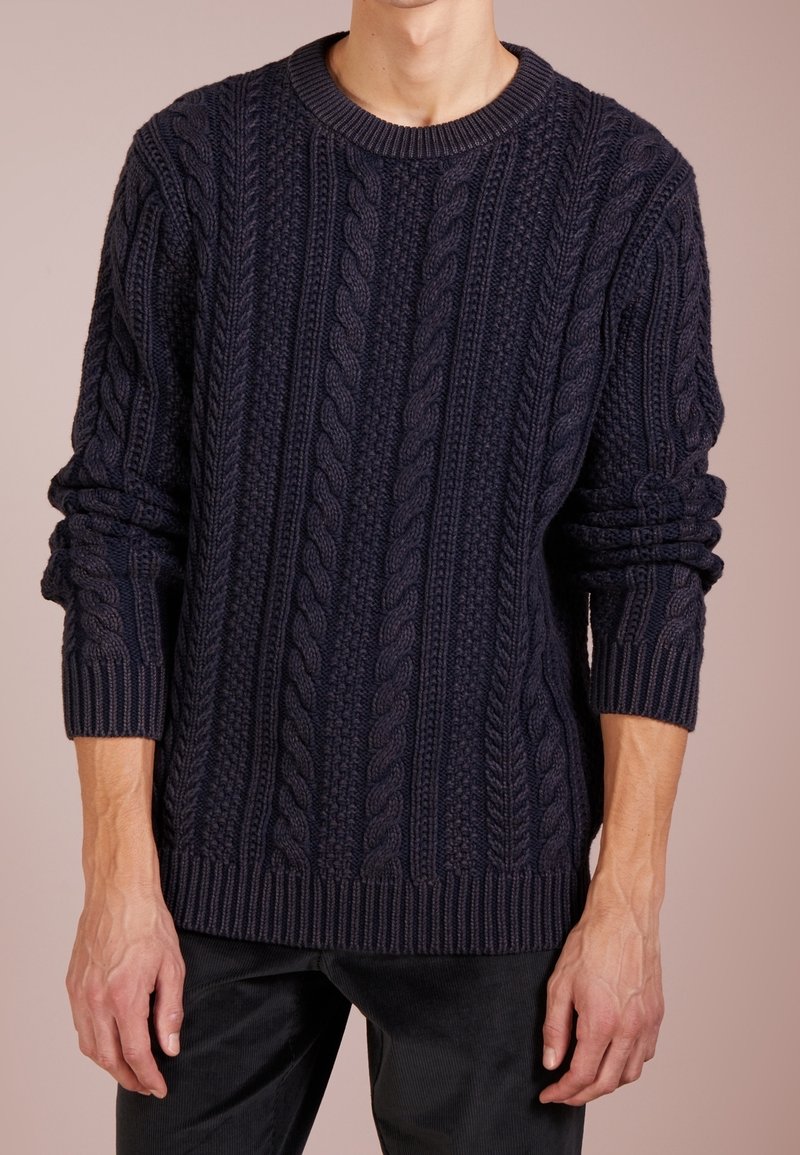 Dunkelblauer Strickpullover mit Zopfmustern, Rundhalsausschnitt sowie gerippten Bündchen und Saum. Hergestellt aus einem dicken, strukturierten Material.