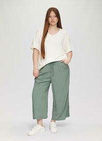 Crème V-hals, losse top gecombineerd met lichtgewicht, mintgroene, brede pijpen met een elastische tailleband en zijzakken, gedragen met witte sneakers.