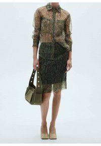 Przezroczysta bluzka w wężowy wzór w ziemistych odcieniach, połączona z dopasowaną spódnicą. Oliwkowa, teksturowana torba na ramię o sztywnej konstrukcji i okrągłych uchwytach.