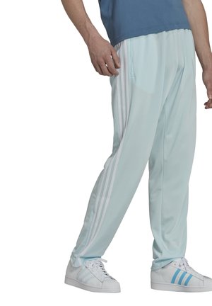 Lyseblå træningsbukser med tre hvide striber ned ad siderne, udstyret med elastisk talje og slim fit, suppleret med hvide sneakers.