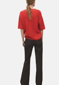 Pull court en maille rouge à manches courtes avec une coupe ample, associé à un pantalon sombre évasé. Contrastes de texture visibles entre les matériaux.