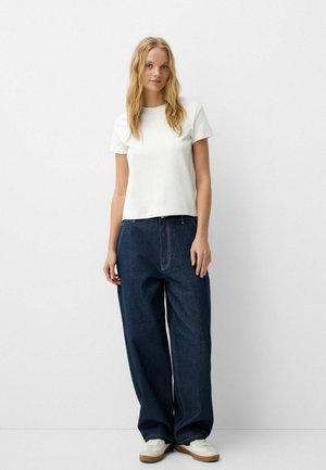 Witte katoenen T-shirt gecombineerd met een losse, donkerblauwe denim jeans. Kenmerkt zich door een eenvoudig ontwerp, rechte snit en minimaal stiksel.