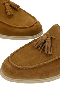 Paire de mocassins en daim marron avec détail pompon et semelles en caoutchouc beige, présentée sur fond blanc.
