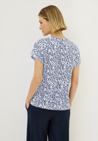 Kortærmet top i hvid med marineblå bladbillede design. Glat stof med en afslappet pasform, rund halsudskæring og en lige kant.