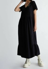 Musta maksimekko lyhyillä hihoilla, V-pääntie, kootut vyötärö ja röyhelöhelma. Yhdistetty vaaleanruskeisiin nilkkureihin, joissa on rei'itetty kuvio.