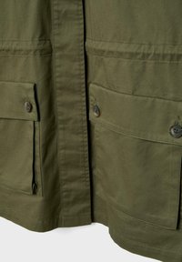 Tissu vert olive avec deux grandes poches à rabat à l'avant, sécurisées par des boutons, situées sur la partie inférieure d'un vêtement.