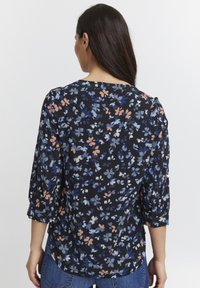 Blusa nera floreale con maniche a tre quarti, caratterizzata da fiori blu, rosa e bianchi in un motivo sparso, tessuto morbido, orlo curvo.