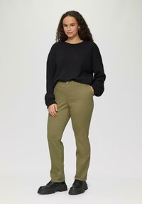 Zwarte, gestructureerde oversized sweatshirt gecombineerd met fitted, olijfgroene broek. Zwarte, stevige veterschoenen maken de outfit compleet. Eenvoudig, casual ontwerp.