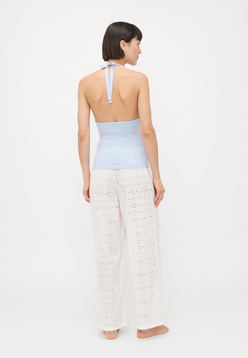 Lichtblauw mouwloos topje met een strikje bij de hals, gecombineerd met witte, wijde broek met uitgesneden bloemmotieven.