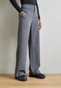 Pantalons à jambes larges gris, taillés, fabriqués en tissu texturé, avec des poches latérales et une fermeture éclair à l'avant. Associés à des chaussures à plateforme noires épaisses.