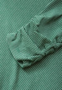 Groen en wit gestreepte stof met een geplooide mouwdetail; gladde textuur; horizontale strepen zijn uniform in breedte.