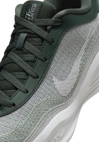 Gros plan sur une chaussure de course Nike verte et gris clair avec des lacets texturés et un logo Nike Swoosh visible sur le côté.