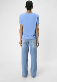 Camiseta de cuello redondo azul claro hecha de tejido suave, combinada con unos pantalones vaqueros de mezclilla clara de tiro alto y pierna ancha, con un acabado desgastado.