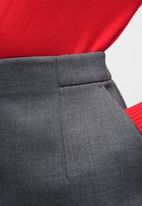 Pantalones a medida grises con una textura suave, que cuentan con un bolsillo frontal plano y una cintura alta, combinados con un suéter rojo acanalado.