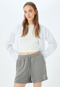 Grijze katoenen shorts met een elastische tailleband en trekkoord, voorzien van zijkanten zakken en geborduurde tekst in het wit. Gepaard met een wit shirt.