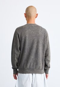 Grå fleece sweatshirt med tekstureret finish, rund halsudskæring, lange ærmer og en ufuldstændig kant, vist fra ryggen.