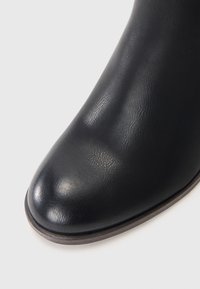 Botín negro de tobillo hecho de cuero sintético texturizado, con punta redonda y un acabado suave y brillante con un ligero brillo.