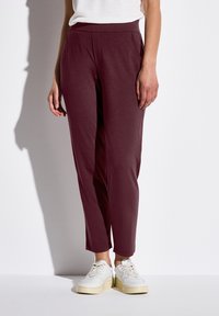 Bordeaux tapered byxor med en mjuk textur, med sidofickor och ett elastiskt midjeband, ihop med vita sneakers.