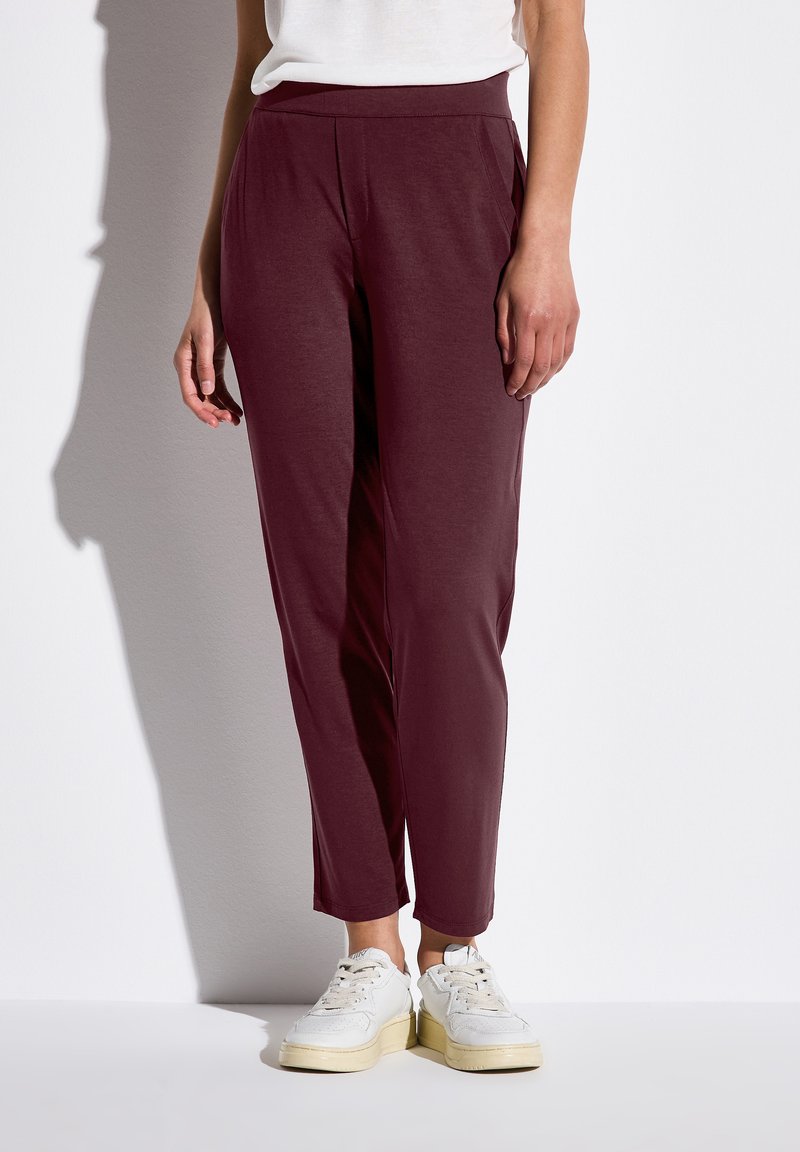 Bordeaux tapered byxor med en mjuk textur, med sidofickor och ett elastiskt midjeband, ihop med vita sneakers.
