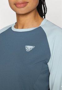 Lühikeste varrukatega sportlik ülemine osa sinises ja helesinises, millel on sile tekstuur ja rinna peal kolmnurkne logo brändingu jaoks.