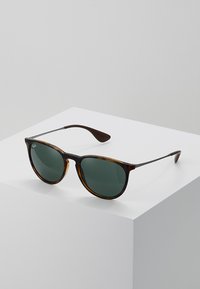 Tortoiseshell zonnebril met groene lenzen, ronde vorm, dunne metalen armen en donkerbruine uiteinden. Minimalistisch ontwerp.