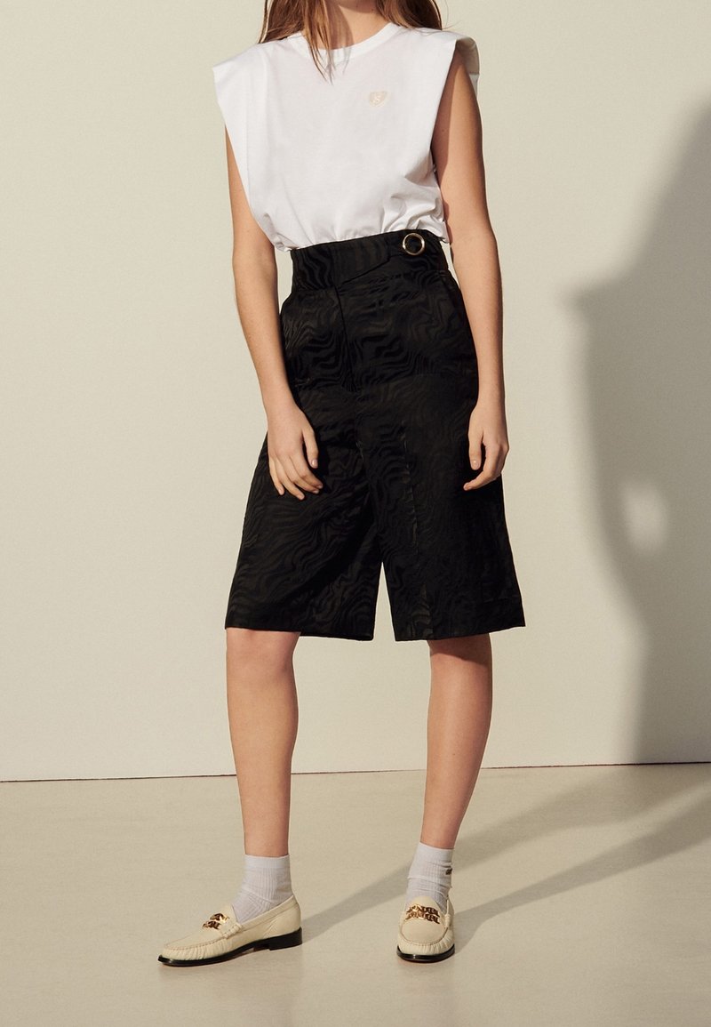 Haut blanc sans manches avec un logo discret, associé à un short noir taille haute à motif texturé et détail ceinture, complété par des mocassins.