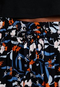 Jupe noire à motifs floraux colorés en bleu, orange et rose, dotée d'une ceinture élastique et d'une fermeture à nouer ajustable.