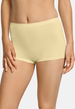 Mujer vistiendo ropa interior tipo boyshort sin costuras de color amarillo claro, vista de la cintura a la mitad del muslo sobre un fondo liso.