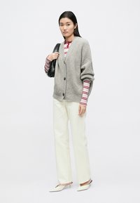 helehall hõlmikdisainiga kampsun soonikkoes, mustade nuppudega, kantud üle punase ja valge triibulise topi, kombineeritud kreemika valgete pükste ja kontsakingadega.