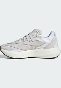 Zapatilla deportiva gris claro con parte superior de malla, acentos de ante, sistema de cordones integrado y una suela blanca gruesa con patrones texturizados.