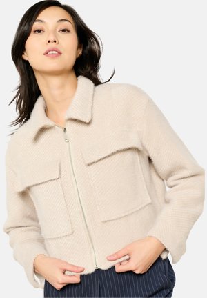Beige, textured jacket with a collar, front zipper, and two chest pockets. Soft material, cropped design, and loose-fit sleeves.