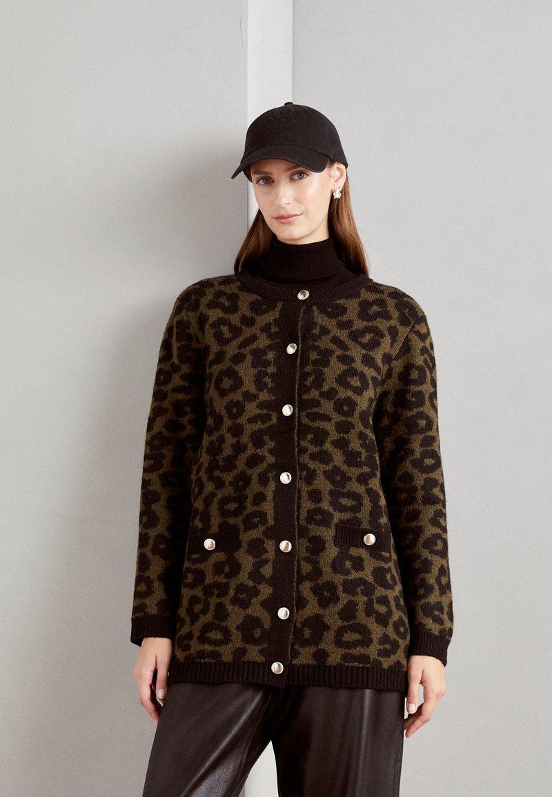 Leopardprint cardigan in donker groen en bruin, met een knopenflap, ribbels aan de onderkant en twee voorzakken. Draagt over een zwarte coltrui.