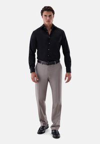 Schwarzes langärmeliges Hemd mit Knopfverschluss, kombiniert mit hellbeigen Hosen. Verfügt über einen Gürtel und schwarze glänzende Lederschuhe.