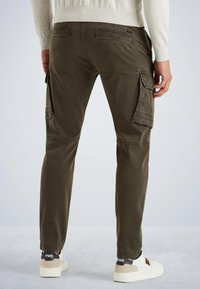 Pantalons cargo vert olive avec plusieurs poches, coupe ajustée et détails cousus, associés à des baskets blanches avec des accents noirs.