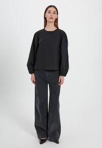 Top nero a collo rotondo con maniche arricciate e dettagli legati. Abbinato a jeans neri a gamba larga e sbiaditi. Design semplice e strutturato.