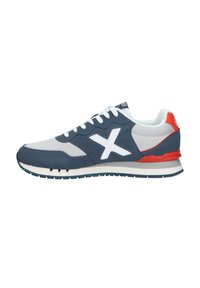 Zapatilla deportiva en azul marino y gris con logo blanco, parte superior de malla y ante, acentos rojos, cuello acolchado y suela media blanca sobre una suela exterior de goma texturizada.
